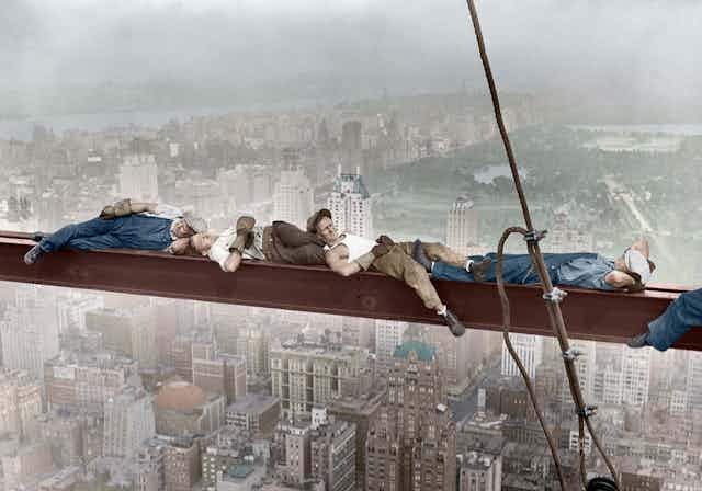 Construction workers rest on a steel beam.