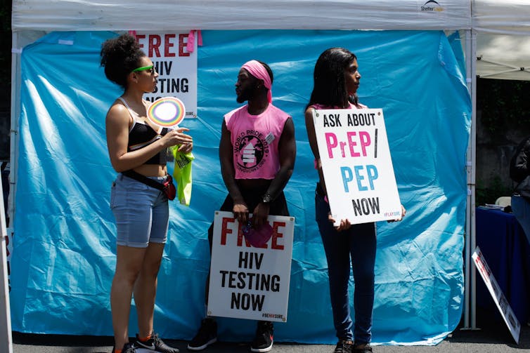 Three people hold signs saying 'Free HIV testing now' and 'Ask about Prep/Pep now.'