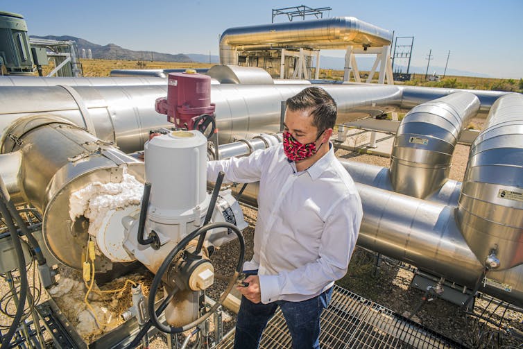 Man examines valve at end of large piping network.