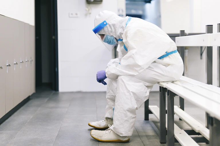 male clinician in white personal protective gear sitting on a bench looking down