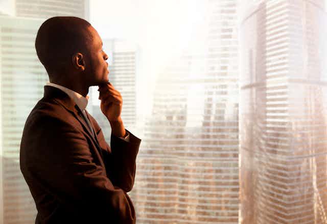 A Black man looks out a window at skyscrapers.