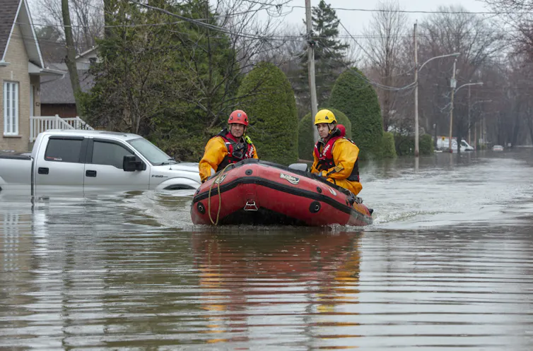 Deux hommes à bord d’un canot pneumatique descendent une rue inondée