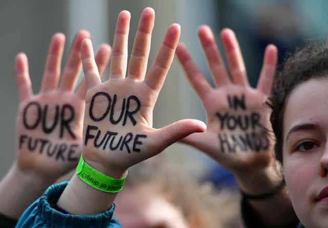 Young protesters with "Our Future" is "In Your Hands" written on their palms.