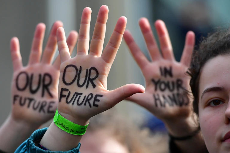 Young protesters with "Our Future" is "In Your Hands" written on their palms.