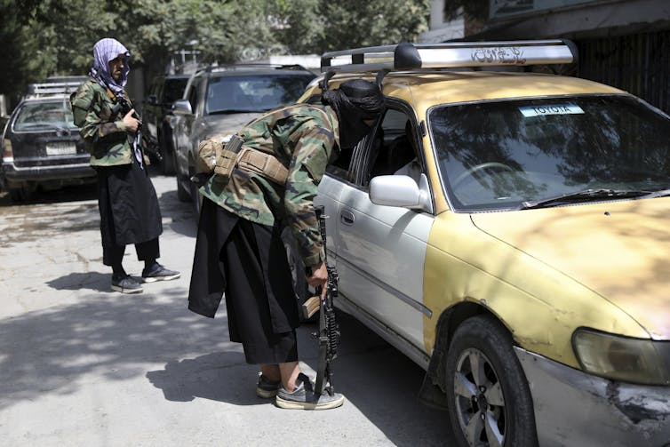 Taliban fighters search a vehicle at a checkpoint in Kabul.