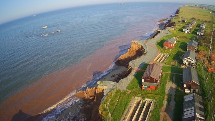 A coastline, edged by houses, showing signs of erosion