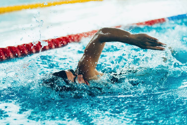 Person wearing a swim cap performs the front crawl in a swimming pool.