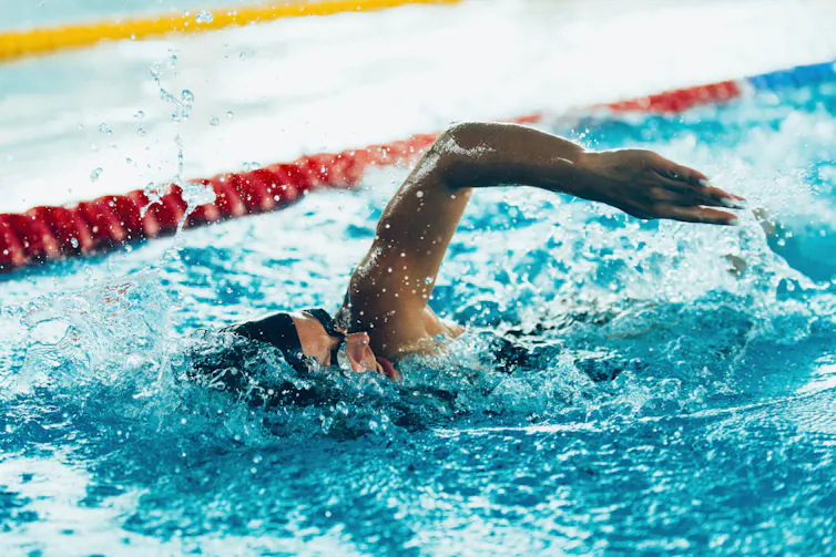 Person wearing a swim cap performs the front crawl in a swimming pool.