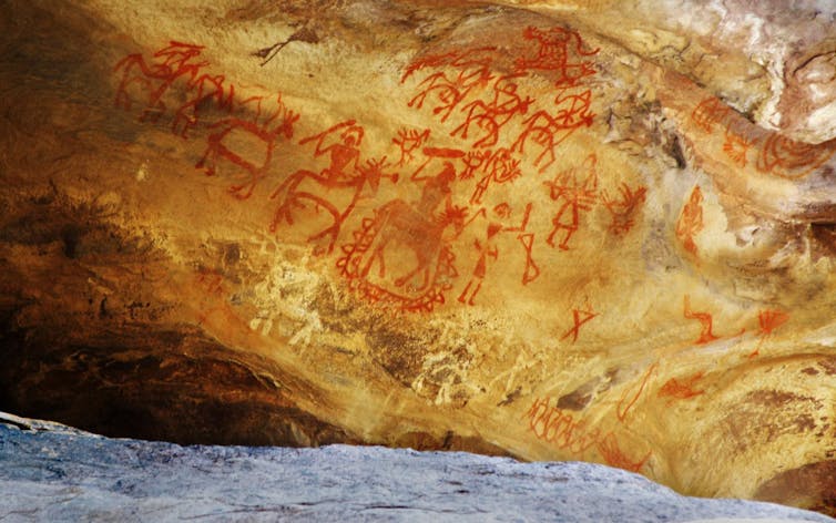 Red paintings of animals and humans on the wall of a cave