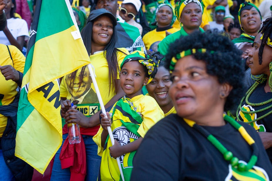 A child carries an ANC flag among jovial women at a rally.