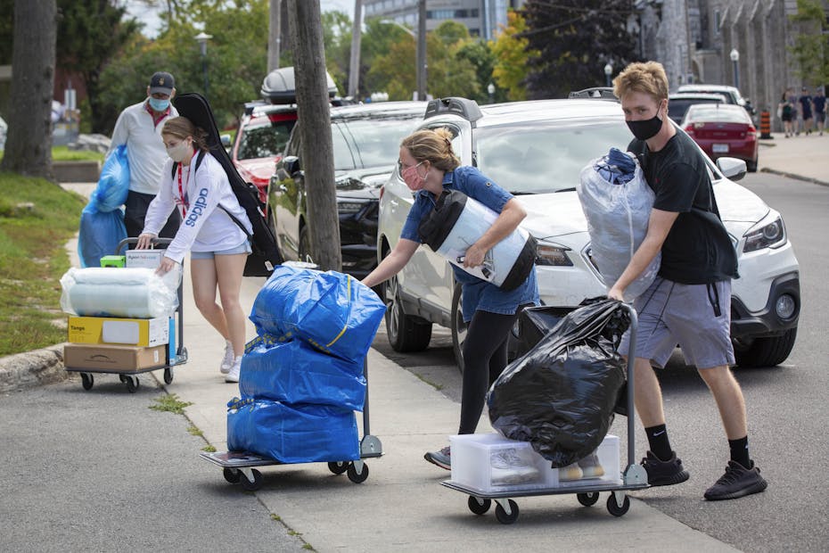 People pushing carts of bags across a driveway.