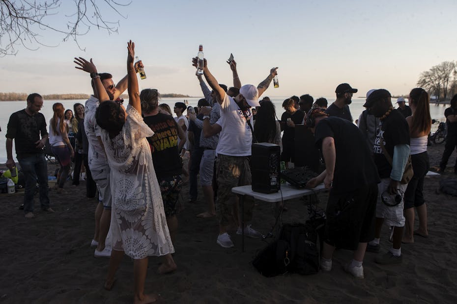 People dancing and drinking on a beach at sunset.