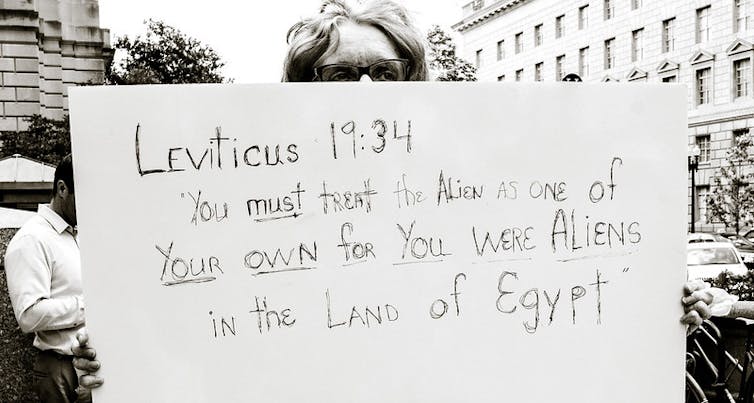 A person holds a sign that says Leviticus 19:34: 