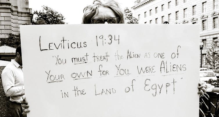 A person holds a sign that says Leviticus 19:34: