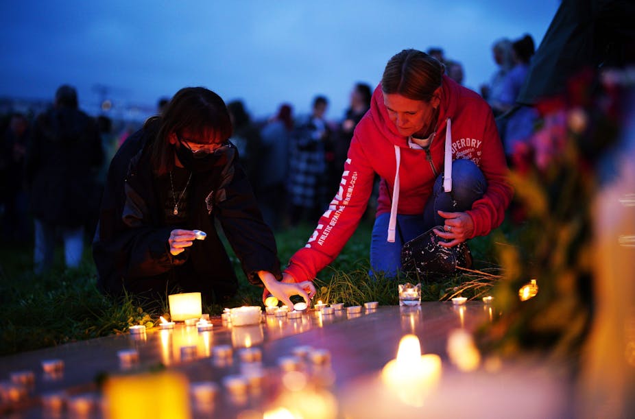 Two people lighting candles at a vigil for the victims of Jake Davison. 