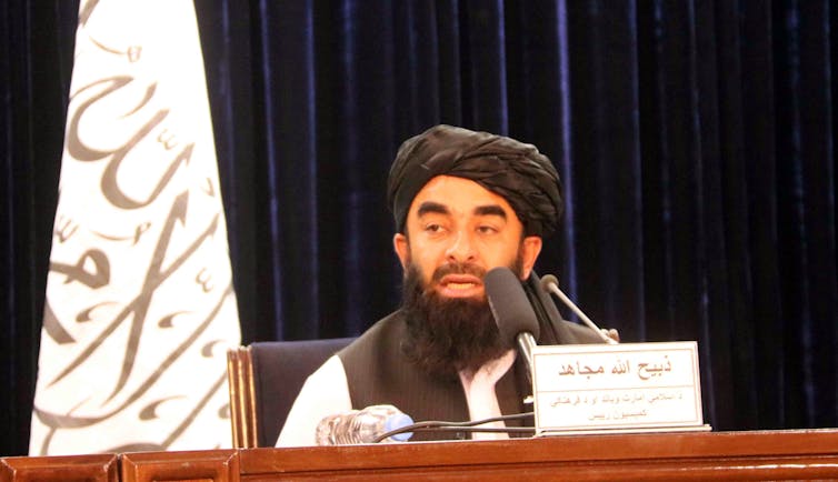 Taliban spokesperson Zabiullah Mujahi talking into a microphone at a press conference.