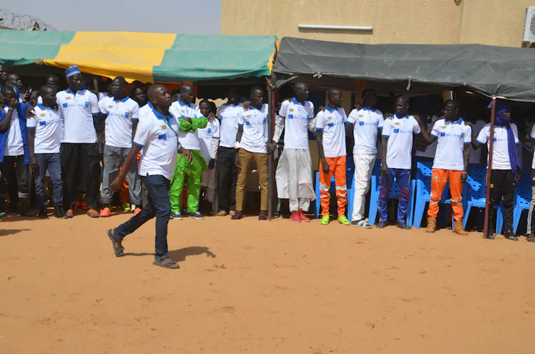 A group of people link arms and stand together in a line as one person walks in front of them