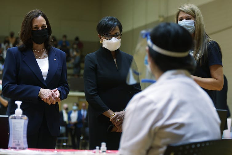 Vice President Kamala Harris, wearing a mask, meets with several people at a pop-up vaccination clinic.