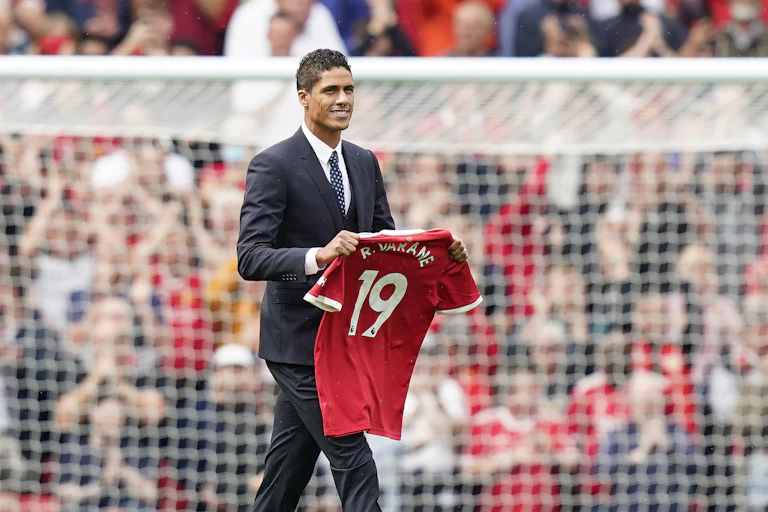 Varane holding his new Manchester United shirt on the pitch.