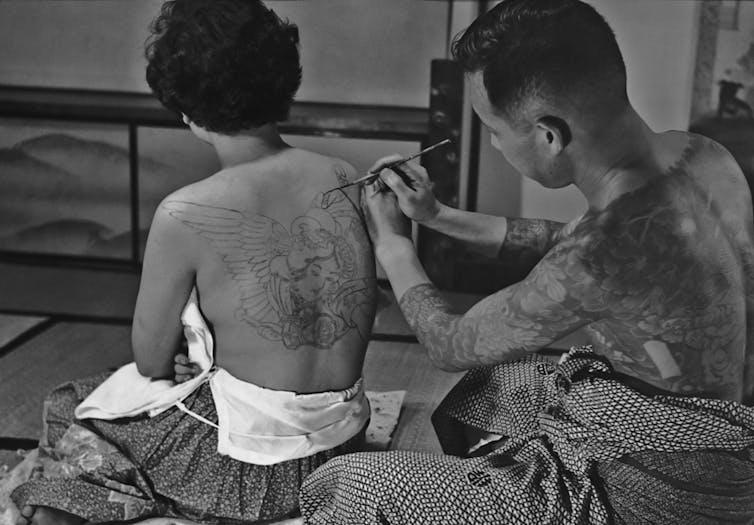 A Japanese tattoo artist at work on a design on a woman's back in Japan in 1955.
