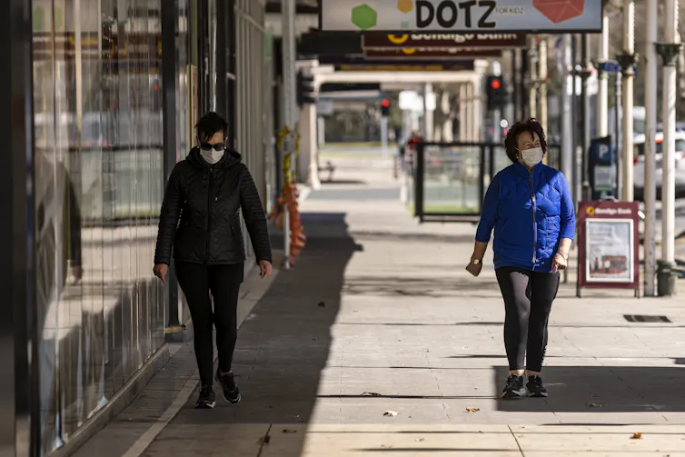 Two people walking on Melbourne's streets in masks, about 1.5 metres apart.
