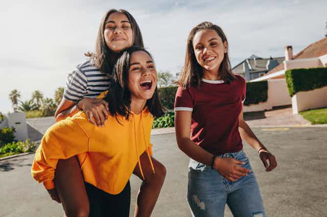 Three smiling teenage girls walking on a suburban street.