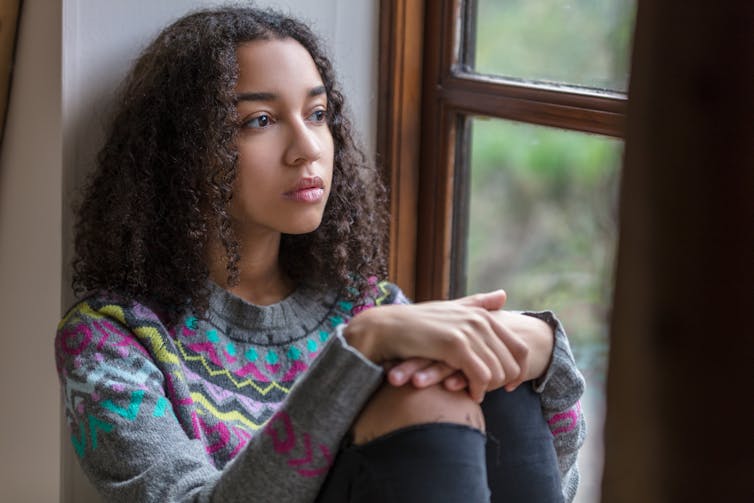 A teenage girl sits looking out a window.