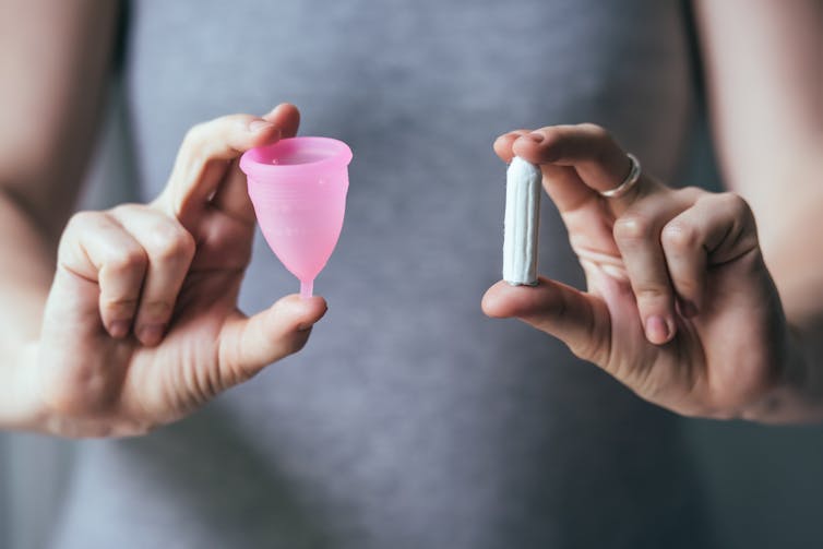 A woman holds a menstrual cup and a tampon.