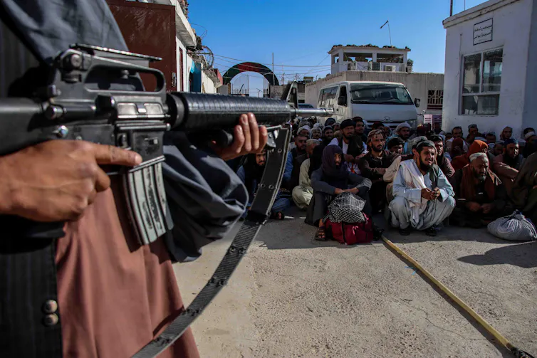 A man with an automatic rifle stands guard over a group of Afghanistani men released from prison in Kabul, August 17 2021.