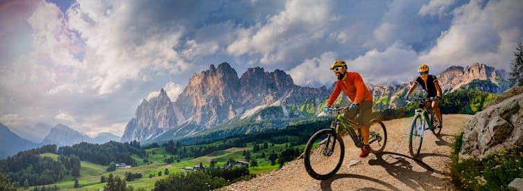 Woman and Man riding on bikes in Dolomites mountains landscape.