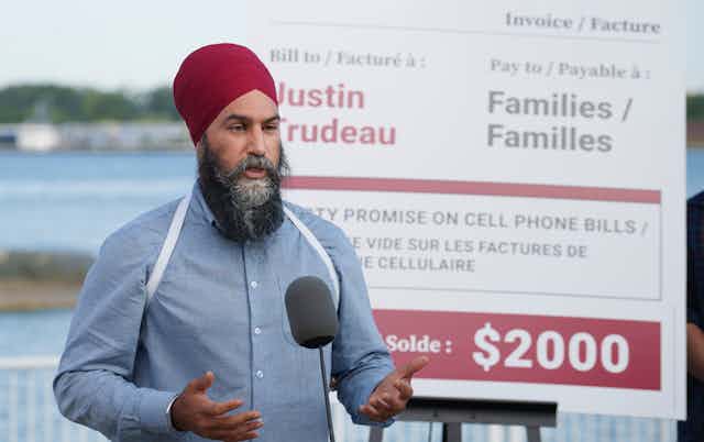 Jagmeet Singh stands before a sign critical of the Liberals.