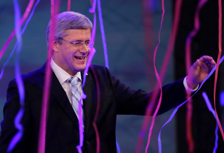 Stephen Harper smiles and waves amid pink and purple streamers.