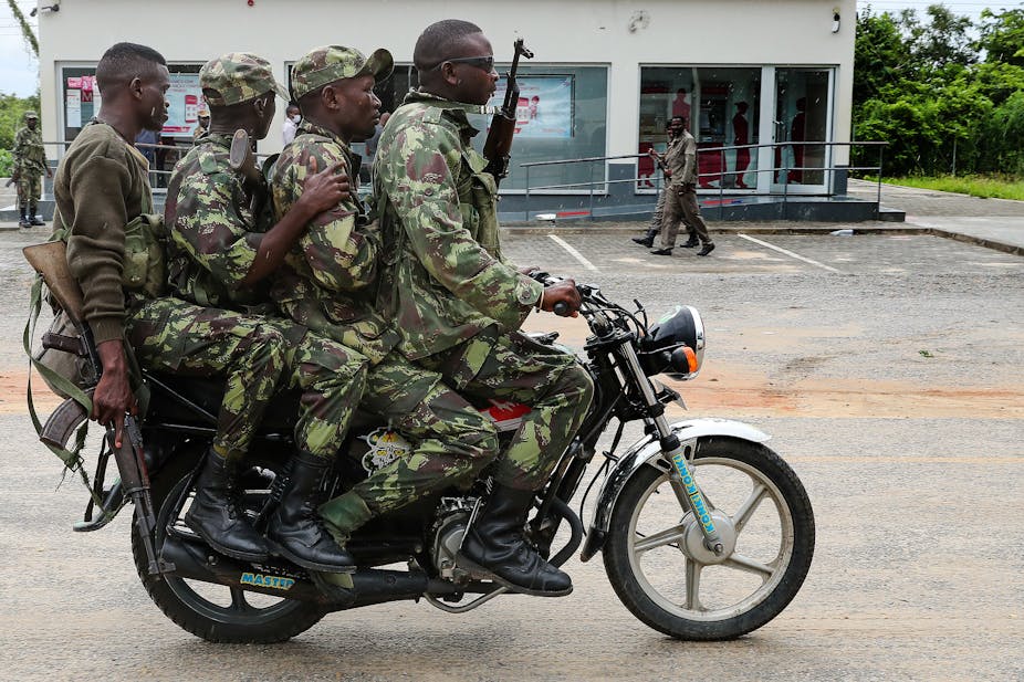 Four men in camouflage uniform and carrying weapons ride a single motorbike 