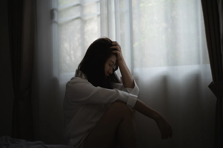 A woman sits on the floor with a hand on her head