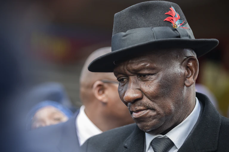 A man wearing a fedora hat with a feather, suit, shirt and tie displays a pensive mood.