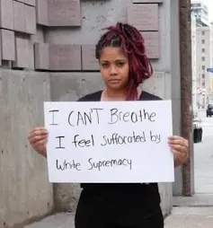 A woman holds a sign up that says 'I can't breathe.'