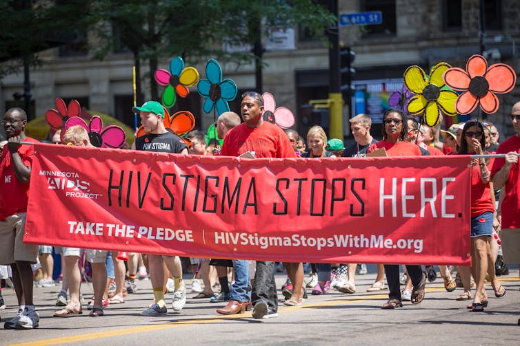 People in a parade carrying a banner that reads 'HIV Stigma Stops Here.'