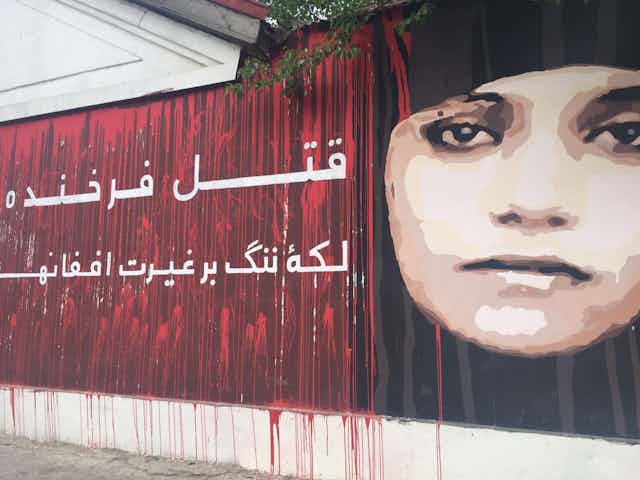 A mural showing the face of an Afghan woman with writing in Arabic alongside it.