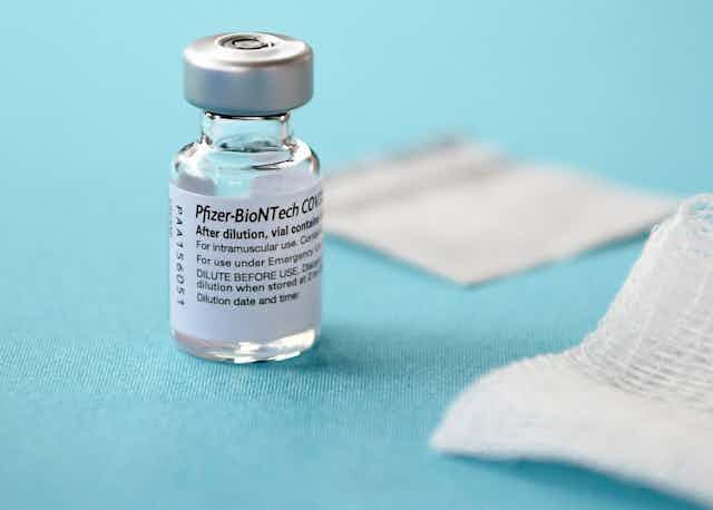 A vial of Pfizer-BioNTech COVID-19 vaccine and white gauze pads on a blue background