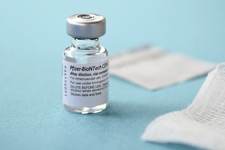 A vial of Pfizer-BioNTech COVID-19 vaccine and white gauze pads on a blue background