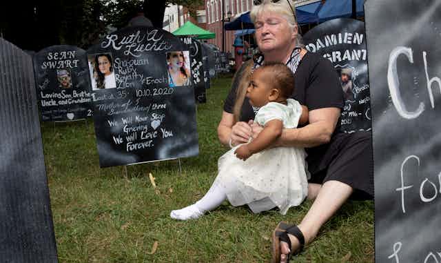 A grandmother hugs her granddaughter in a makeshift graveyard created by anti-opioid protesters.