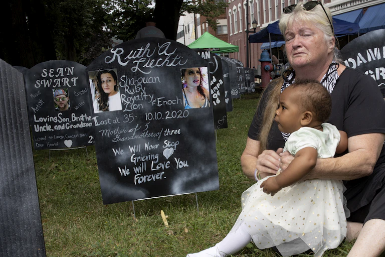 A grandmother hugs her granddaughter in a makeshift graveyard created by anti-opioid protesters.