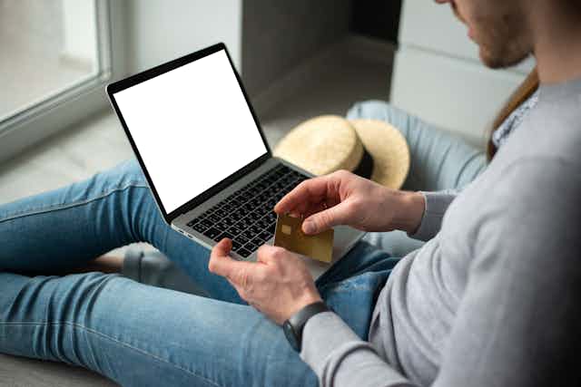 young man with laptop on his knee holds a credit card ready to make an online payment