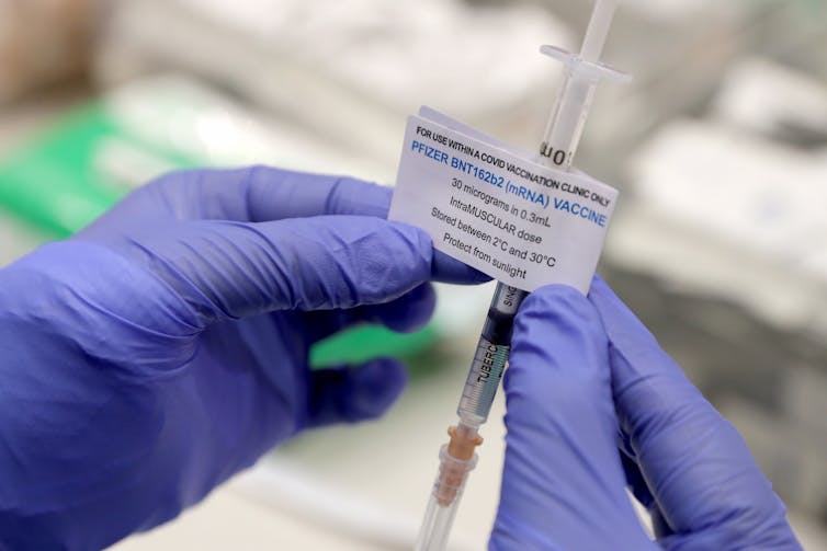 Gloved hands prepare a Pfizer vaccine.