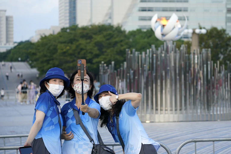 Three Tokyo Olympics volunteers posing for a selfie in front of the Olympic flame
