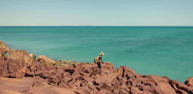 A man walking on rocks near the ocean.