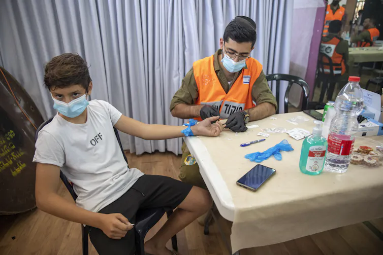 A boy receives an antibiody test from a solidier at a table.