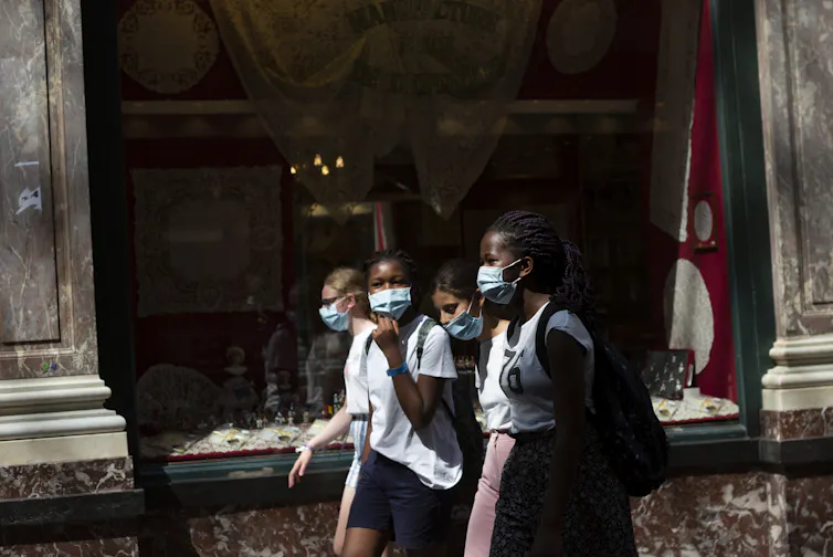 Girls walk wearing face masks on a street.