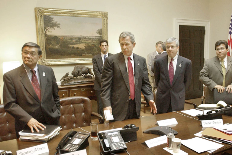 Men in suits stand around a meeting table