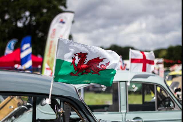 A welsh flag flying out of a car window and an English flag flying out of another car window in the background. 